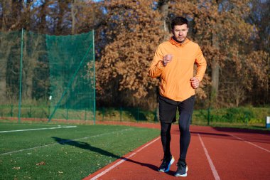 Turuncu spor ceketli bir adam stadyumda koşuyor. Dayanıklılık eğitimi kavramı