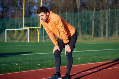Turuncu spor ceketli bir adam, elleri açık koşu pistinde öne eğiliyor. Antrenman kurtarma kavramı