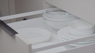 Kadın elinin mutfak çekmecesine kase ve bulaşıklarla birlikte beyaz tabaklar koyması. Mutfak organizasyonu kavramı