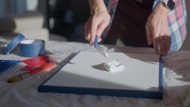 Stüdyoda çalışma masasındaki aletleri kullanarak tuvale desenli macun süren bir kadın. Dokulu sanat yaratımı kavramı