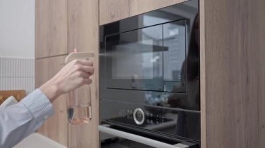 Kadın mutfaktaki mikrodalga fırın kapağına şişeden sıvı püskürtüyor. Ev temizliği ve hijyen kavramı