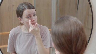 Evde banyo aynasına bakarken cilt kremi süren bir kadın. Günlük cilt rutini kavramı