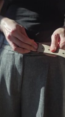 Güneş ışığında kadın kemerini gri pantolona bağlarken. Günlük giysi ve günlük kıyafet kavramı
