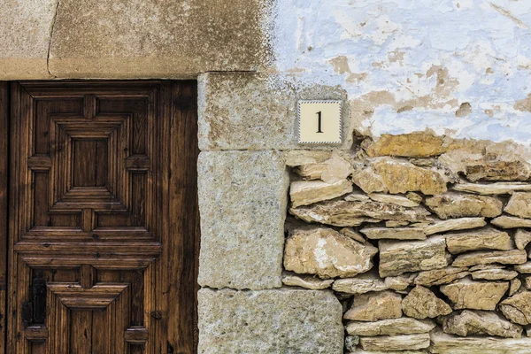 Parede de rocha fachada com porta de madeira e placa número um — Fotografia de Stock