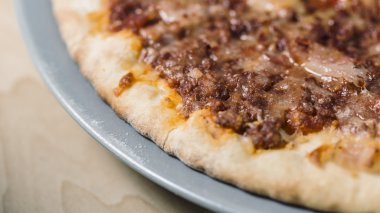 Ahşap bir masa üzerinde mavi bir tabak üzerinde pişmiş pastırma et pizza