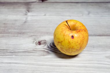 Yalnız sarı sonbahar elması meyvesi, ahşap bir arka planda hala izole bir şekilde duruyor.