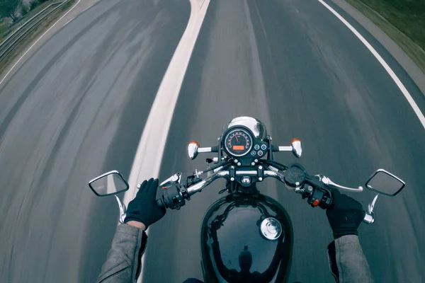 Asfalt yolda hız göstergesi olan eski siyah bir motosiklete binmek.