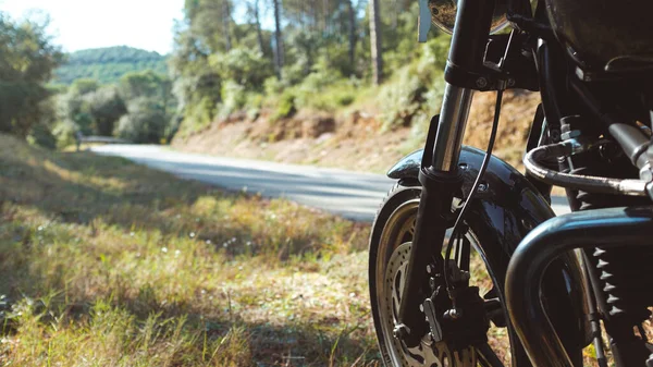 Black motorbike parked next to the edge of a road on a green mountain landscape winding road