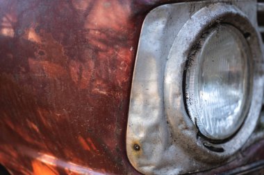 Kırmızı tozlu ve paslı bir arabanın ön lambasının ayrıntıları.