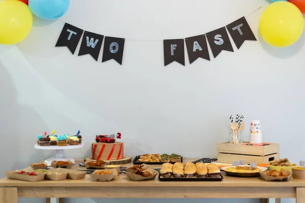 Farklı aperatifler ve tatlı yiyecekler bir doğum günü partisinde ahşap bir masada servis edilir.