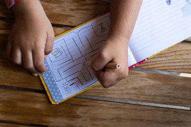 Çocuk eller tahta masaya not defterine çizgiler çiziyor.