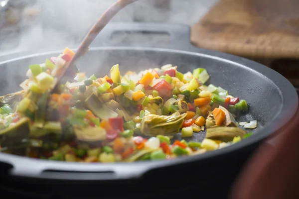 Wood spoon mixing veggies on a pan