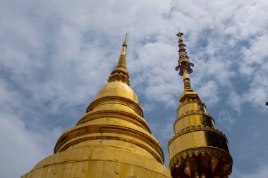 Tayland 'daki Chiang Rai tapınağında bulutlu bir gökyüzünde altın renkli pagodalar.