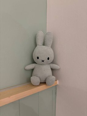 Yumuşak yumuşak ve pürüzsüz yeşil gri tavşan oyuncağı aynı renk desenlere sahip bir duvar köşesinde