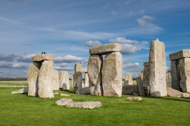 Stonehenge, Cotswolds 'daki güzel mavi bulutlu gökyüzünün altında yeşil bir tarlada bulunan ünlü İngiliz tarihi simgesi.