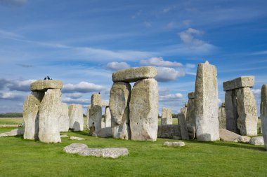Stonehenge, Cotswolds 'daki güzel mavi bulutlu gökyüzünün altında yeşil bir tarlada bulunan ünlü İngiliz tarihi simgesi.