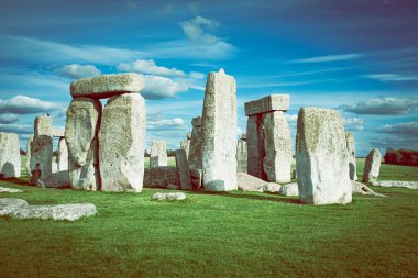 Stonehenge, Cotswolds 'daki güzel mavi bulutlu gökyüzünün altında yeşil bir tarlada bulunan ünlü İngiliz tarihi simgesi.