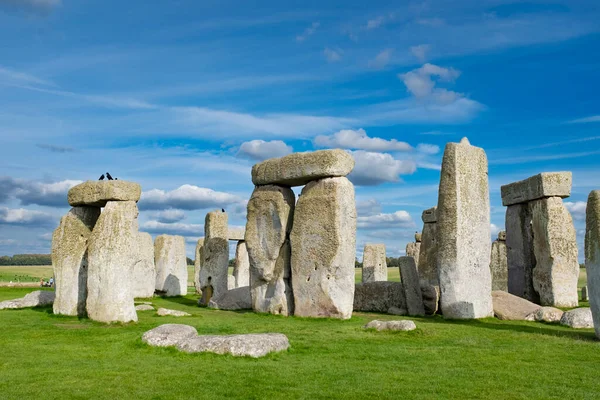 Stonehenge, Cotswolds 'daki güzel mavi bulutlu gökyüzünün altında yeşil bir tarlada bulunan ünlü İngiliz tarihi simgesi.