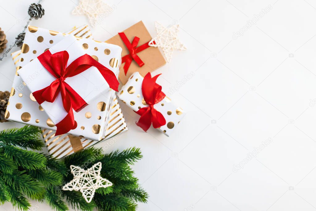 A white and gold gift boxes with a red ribbon bow and Christmas tree branches and star on a light background with copy space. Top view, flat lay. Xmas decoration, festive backdrop.