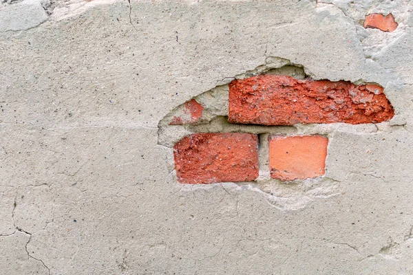 Old wall with a hole from fallen off plaster and red brickwork. Broken gray cement surface with cracks. Facade of an ancient industrial building, background with copy space.