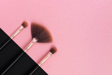 Pembe ve koyu arkaplanda üst üste profesyonel makyaj fırçaları. Siyah ve gül rengi makyaj sanatçıları için aletler. Kadınlar için kozmetik, güzellik konsepti, cilt bakımı. Boşluğu kopyala.