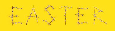 Yumuşak söğüt dalları sarı arka planda Paskalya kelimesine katlanır. Bahar minimalist kompozisyonu, web afişi. Geleneksel dekorasyon ve Palm Sunday konseptiyle Nisan tatili. Üst görünüm.