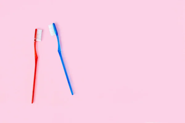 コピースペースのピンクの背景に2つの青と赤の歯ブラシ 男性と女性の個人的な口腔衛生ブラシ カップルのための朝のルーチン バレンタインデー愛のコンセプト — ストック写真