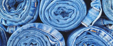 Denim doku afiş arkaplanı. Bir grup mavi kot bir tüp içine sarılmış, çeşitli rahat pantolonlar ve kıyafetler. Turuncu iplikli ve dikişli pamuk kumaş..