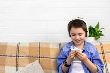 Evde telefon kullanan kulaklıklı genç bir öğrenci. Bir çocuk akıllı telefona bakar, müzik dinler, sosyal medyada film veya video izler, dil öğrenir. Teknoloji, internet, çocuklar için boş zaman.