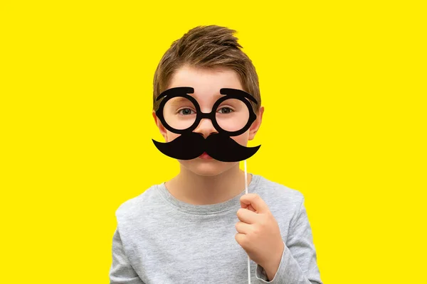 Komik mutlu çocuk elinde siyah hippi bıyığı ve gözlüklü fotoğraf malzemesi tutuyor çocuk sarı arka planda baba, profesör ya da inek gibi davranıyor Babalar Günü konsepti, erkek sağlığı, akıllı çocuklar, şaka, duygu.