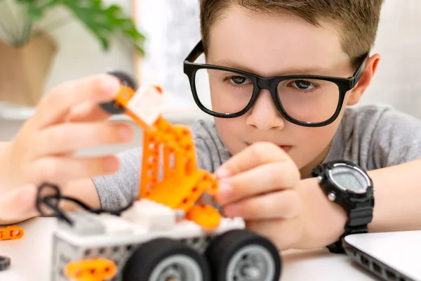 Gözlüklü zeki bir çocuğun evde bir robot araba yapıp programlaması. Çocuk kodlamayı ve programlamayı öğreniyor. Robot Bilimi, Matematik, Mühendislik, Teknoloji. STEM eğitimi