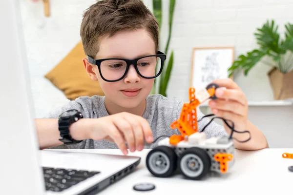 Çocuk dizüstü bilgisayarda kodlamayı ve programlamayı öğreniyor. Çocuk, robot arabaya yoğunlaşarak bakıyor ve kontrol sensörlerini tamir ediyor. Robot bilimi, matematik, mühendislik, teknoloji. STEM eğitimi