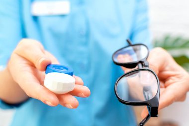 Kadın doktor ellerini tutuyor ve bir klinikteki veya optik dükkandaki hastaya bir çift lens ve gözlük veriyor. Oftalmoloji, görüş düzeltme ve koruma, göz sağlığı konsepti.