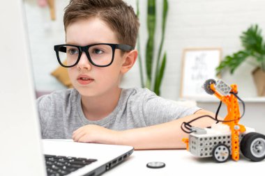 Clever boy builds and programs a robot car using a laptop at home. The child is learning coding and programming. Robotics, Science, Mathematics, Engineering, Technology. STEM education.