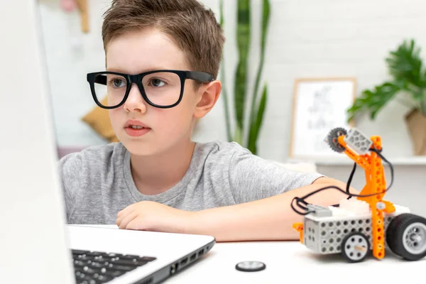 Chico inteligente construye y programa un coche robot utilizando un ordenador portátil en casa. El niño está aprendiendo programación y codificación. Robótica, Ciencia, Matemáticas, Ingeniería, Tecnología. Educación STEM. — Foto de Stock