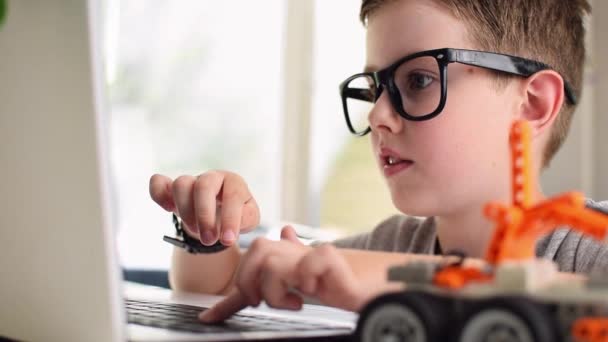 Sidovy av leende smart pojke i glasögon program en robot bil med hjälp av en bärbar dator hemma. Kid lära sig kodning och programmering. Robotik, naturvetenskap, matematik, teknik, teknik. STEM-utbildning — Stockvideo