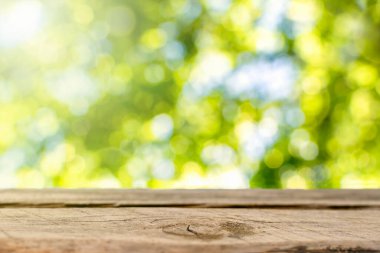 Ağaç yapraklarının ve güneş ışığının bulanık yeşil arka planındaki ahşap masa. Ürün görüntüleme veya görsel tasarım için boş stand sayacı.