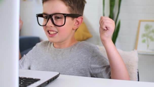 Šťastný mladý běloch, který nosí brýle, má videohovor za použití notebooku, zatímco sedí doma u stolu, usmívá se a mává rukama a mluví o svém úspěchu.. — Stock video