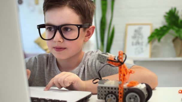 Mądry chłopak w okularach programuje robota używając laptopa i naprawia szczegóły. Dziecko uczy się programowania i programowania w domu. Robotyka, Nauka, Matematyka, Inżynieria, Technologia. Kształcenie STEM — Wideo stockowe