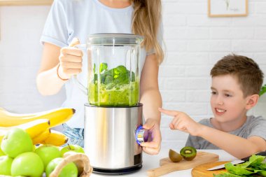 Oğlu, annesinin ev yapımı ıspanak ve meyve arınma suyunu karıştırıcı kullanarak yapmasına yardım ediyor. Genç bayan ve oğlan evdeki mutfakta birlikte meyve püresi hazırlıyorlar. Sağlıklı yiyecek içeceği ve yaşam tarzı konsepti.