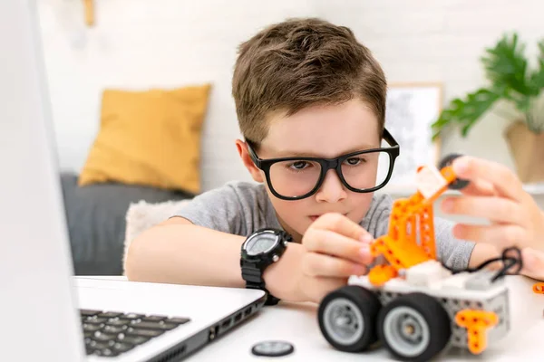 El niño aprende codificación y programación en una computadora portátil. Boy mira con concentración al coche robot y fija los sensores de control. Robótica, ciencia, matemáticas, ingeniería, tecnología. Educación STEM — Foto de Stock