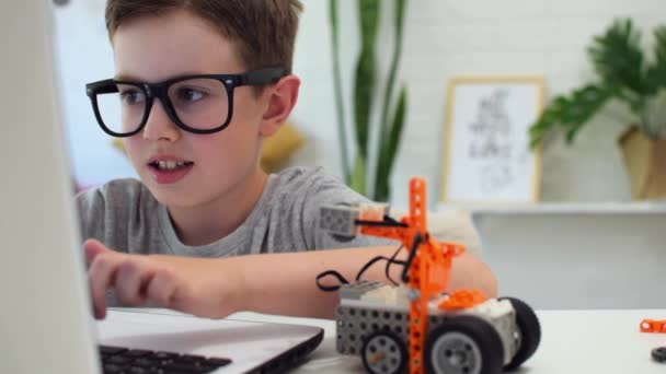 Έξυπνο αγόρι φτιάχνει και προγραμματίζει ένα αυτοκίνητο ρομπότ χρησιμοποιώντας ένα φορητό υπολογιστή στο σπίτι. Το παιδί μαθαίνει κωδικοποίηση και προγραμματισμό. Ρομποτική, Επιστήμη, Μαθηματικά, Μηχανική, Τεχνολογία. STEM εκπαίδευση. — Αρχείο Βίντεο