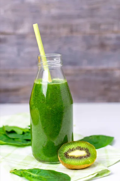 A bottle of spinach smoothie on a brown wooden background, organic green vegetable and fruit juice in a glass with a straw, a vitamin drink for a healthy eating and lifestyle, diet and slim.