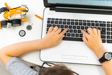 Tanımlanamayan, gözlüklü genç bir çocuk robot bir araç yapıp programlıyor. Elektronik bir oyuncak. Fen dersinde dizüstü bilgisayar kullanan, elleri klavyede yazan bir çocuk. Programlama dersi.