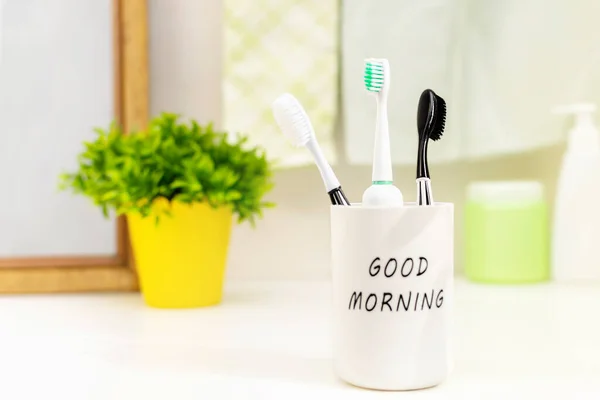 3家族の歯ブラシは 晴れた朝にバスルームカウンターの白いガラスの中に立っています 毎日の歯科衛生 ルーチンと口腔ケアとケアの予防の概念 — ストック写真