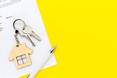 Keys with house shaped keychain and pen on real estate mortgage loan document, contract agreement to buy and construction new home, insurance, lease or rent apartments. Yellow background, copy space. clipart