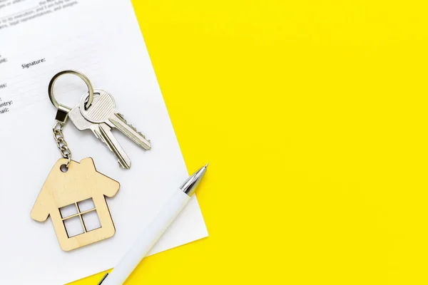 Ev şekilli anahtarlık ve kalemle gayrimenkul ipoteği kredi belgesi, yeni ev, sigorta, kiralama veya kiralık daire satın alma ve inşa etme sözleşmesi. Sarı arkaplan, boşluğu kopyala.