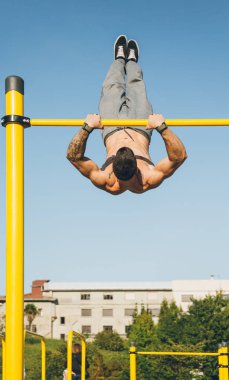 Genç sporcu, açık havada bir spor salonunda barlarda jimnastik yapıyor.