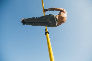 Genç sporcu, açık havada bir spor salonunda barlarda jimnastik yapıyor.