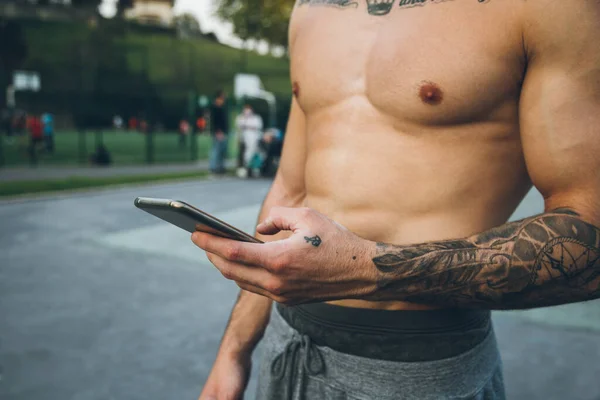 Joven Culturista Urbano Con Tatuajes Usando Teléfono Inteligente Durante Entrenamiento —  Fotos de Stock